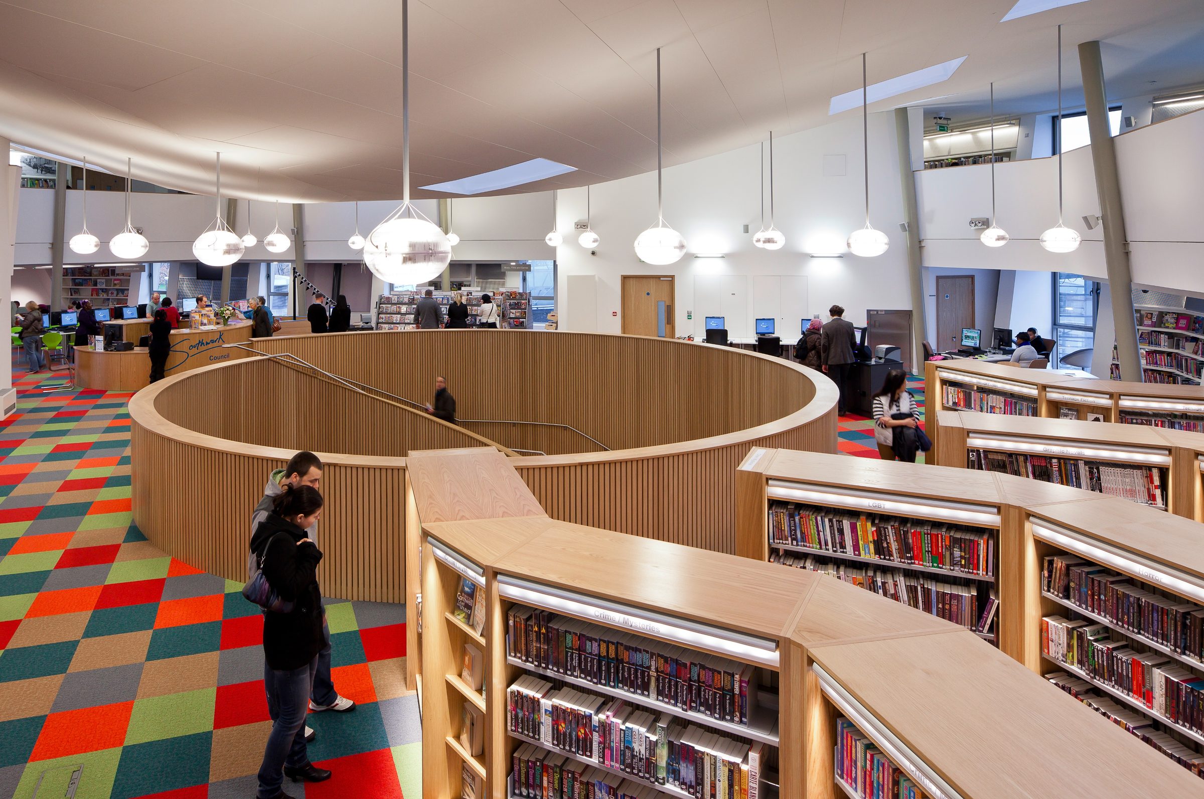 Bookshelves and coloured carpet around the circular stair opening on Canada Water Library's main floor