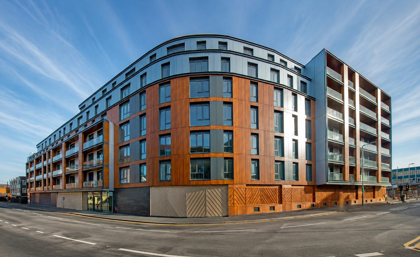 Street view of Nobel House's curved corner, with copper-toned and grey cladding above a dark brick base, Redhill